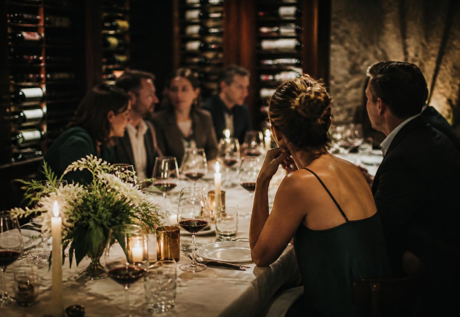 Guests in conversation around a candlelit table in a wine cellar